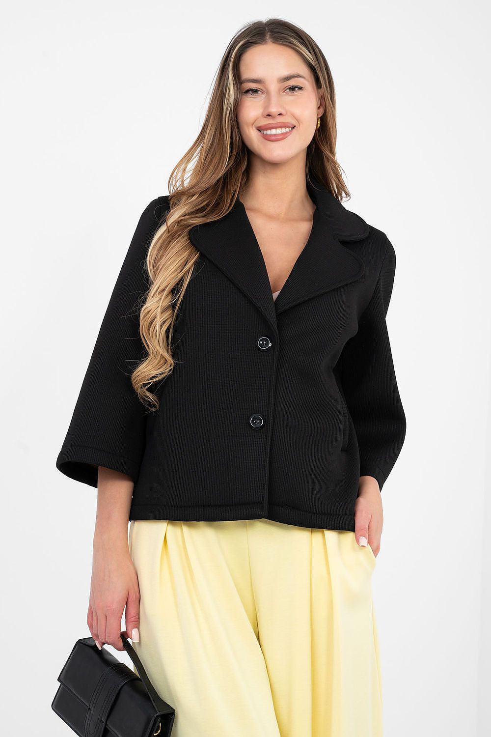 Woman wearing a black jacket and yellow pants against a white background