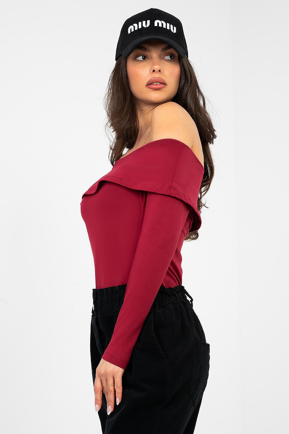Woman wearing a red off-shoulder top and black cap with 'Miu Miu' logo on a white background
