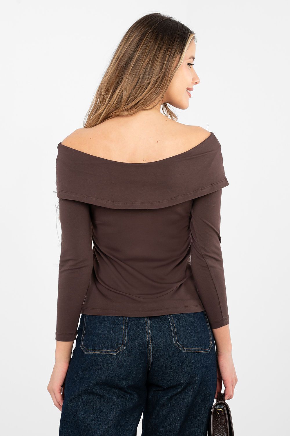 Woman wearing a brown off-shoulder top and dark jeans on a white background