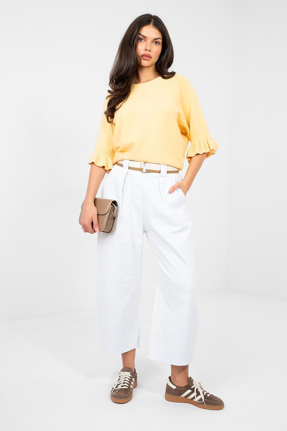 Woman wearing a yellow blouse and white pants with a neutral background