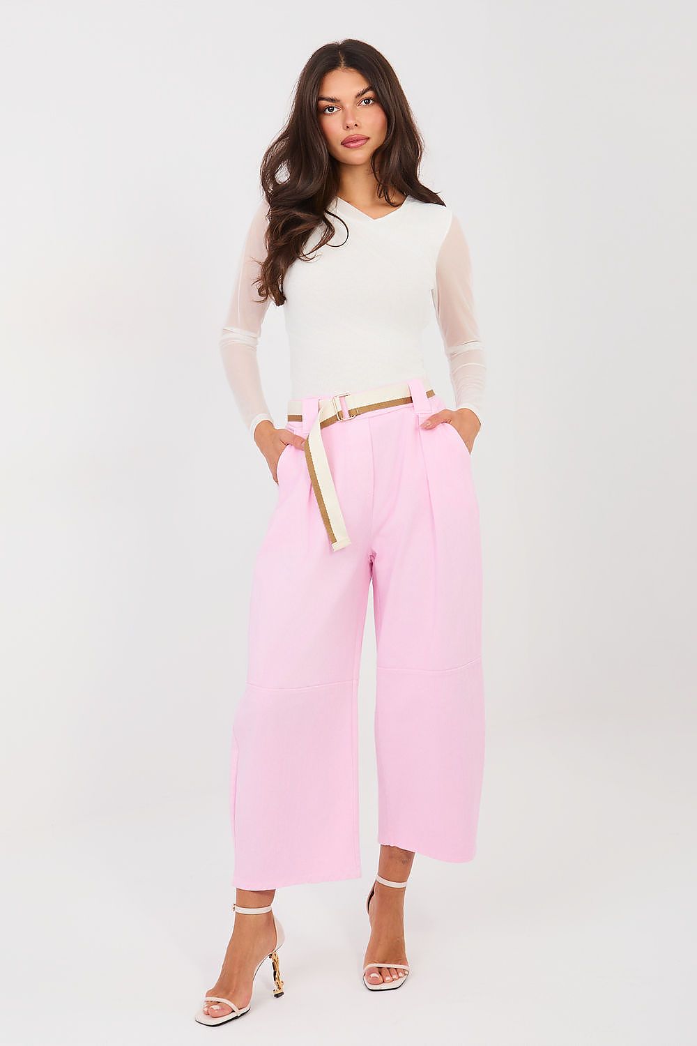 Woman wearing a white top and pink pants with a gold belt on a white background