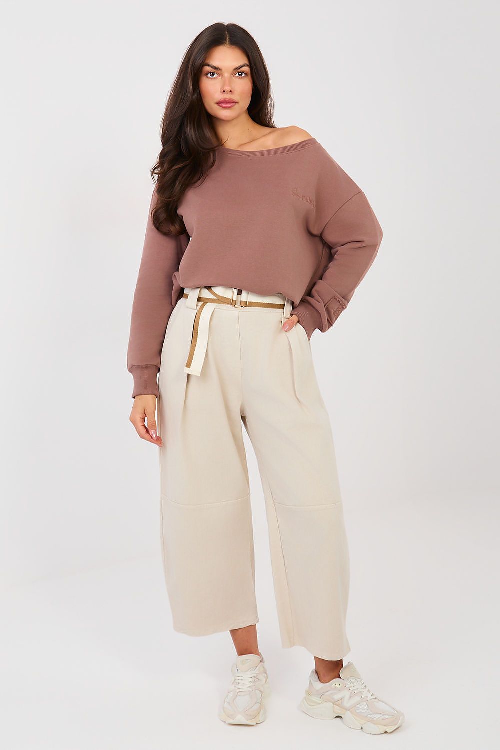Woman wearing a brown off-shoulder sweater and beige pants on a white background