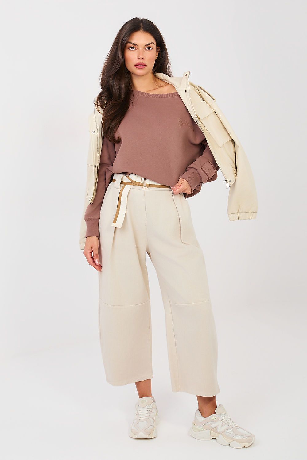 Woman wearing a brown top, beige pants, and a cream jacket on a white background