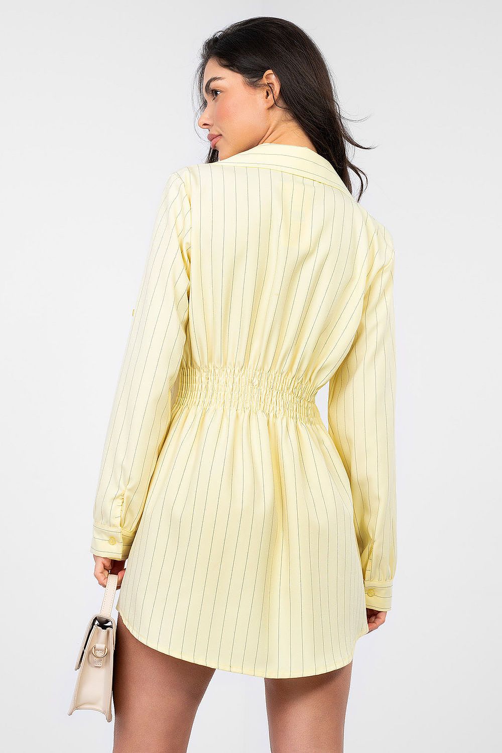 Woman wearing a light yellow pleated dress against a white background