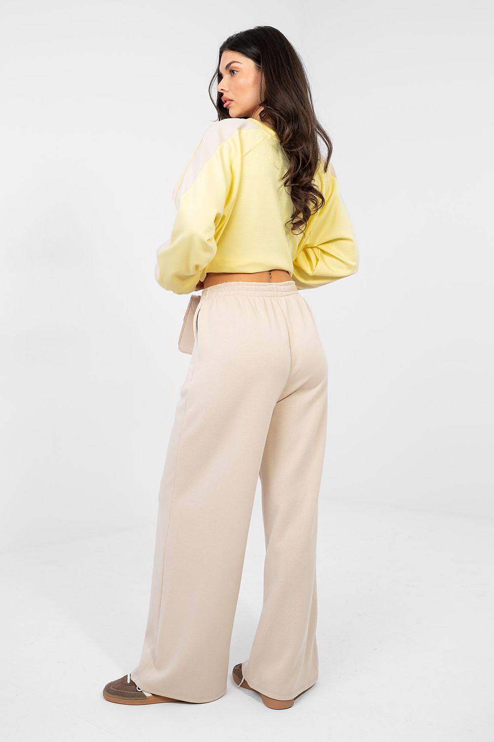 Woman wearing a yellow jacket and beige pants on a white background