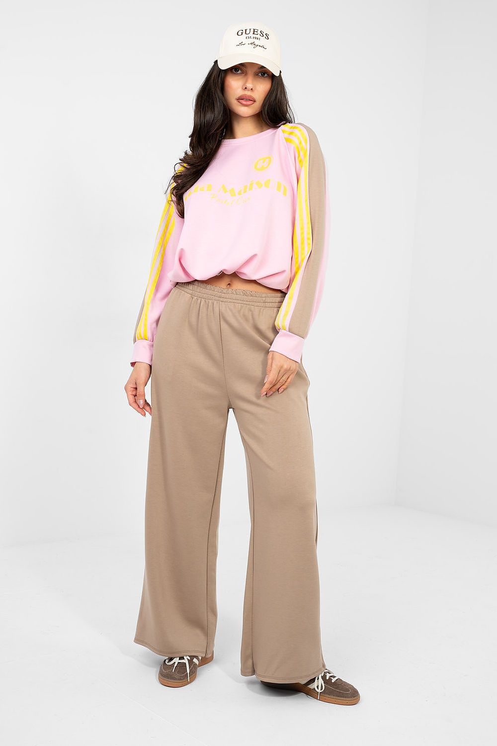 Woman wearing a pink sweatshirt with yellow accents and beige pants on a white background
