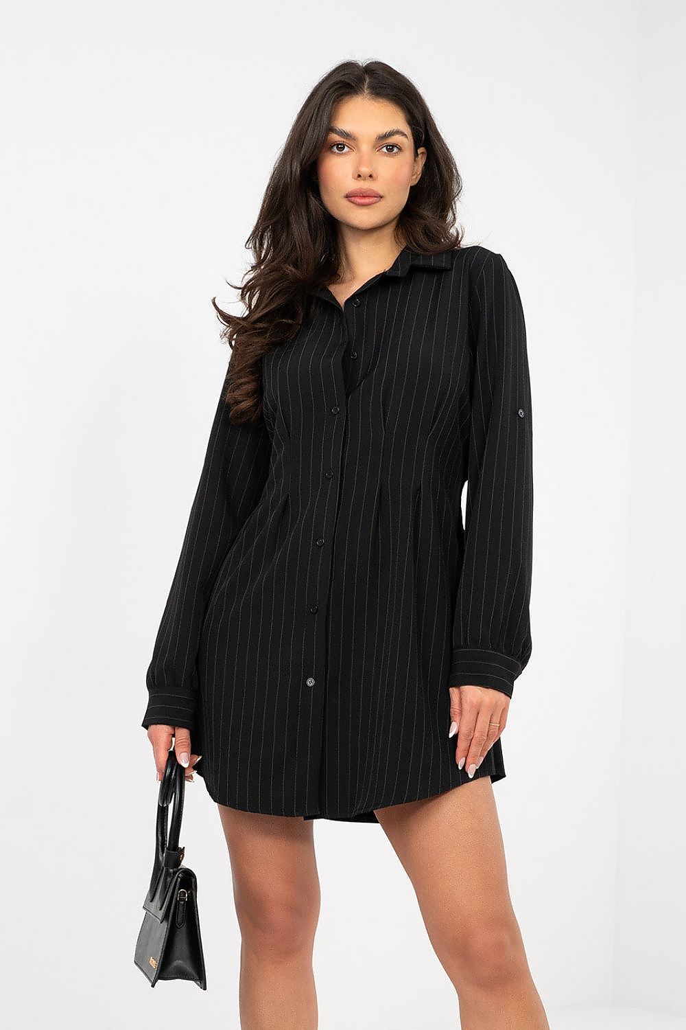 Woman wearing a black ribbed dress holding a black handbag on a white background