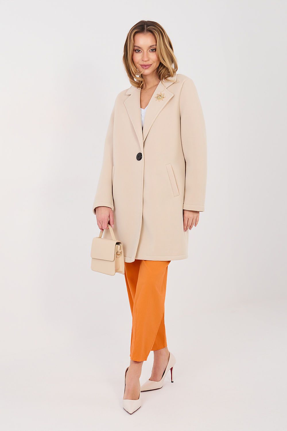 Woman wearing a beige coat and orange pants on a white background