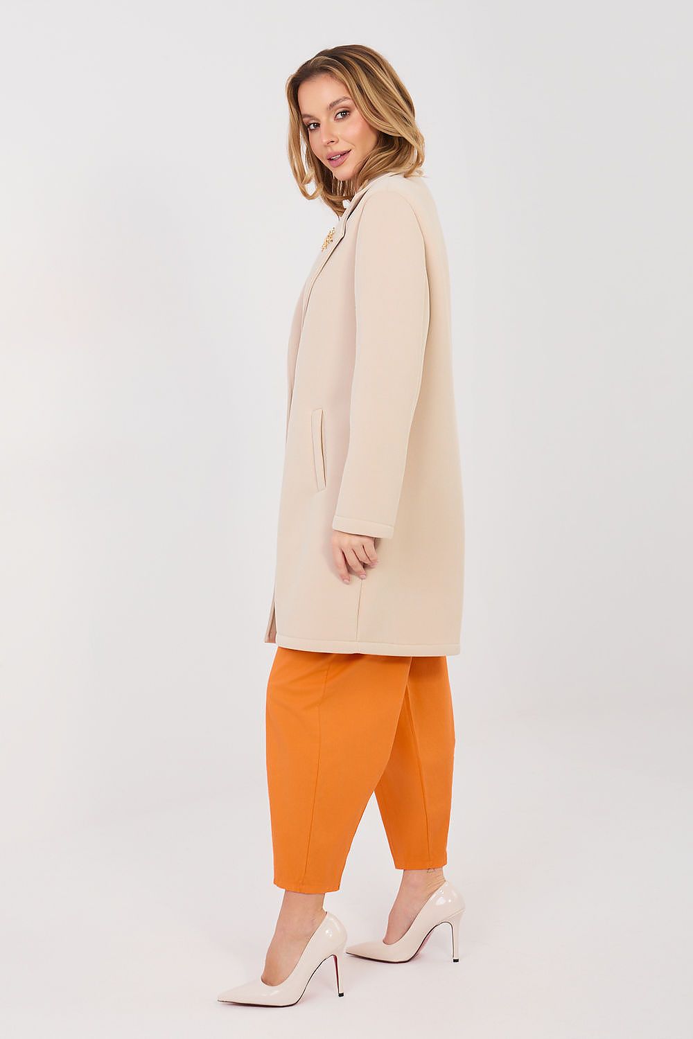 Woman wearing a beige coat and orange pants on a white background