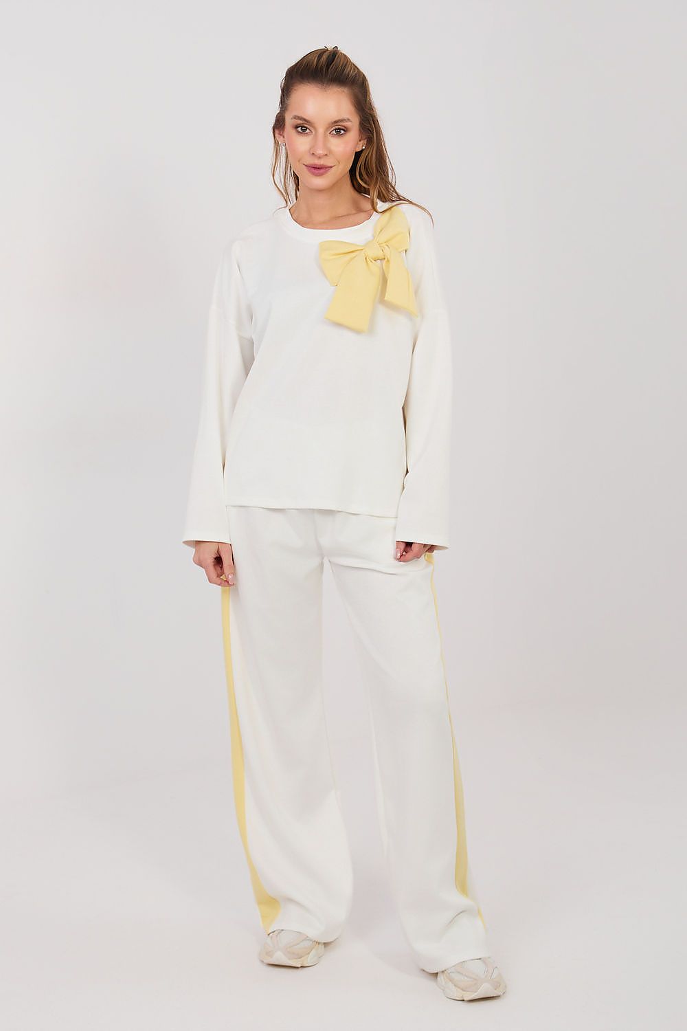 Woman wearing a white outfit with yellow accents on a plain background