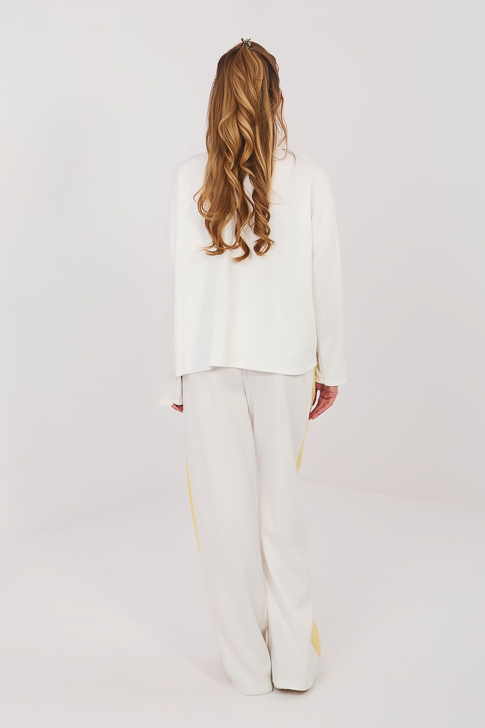 Person wearing a white outfit with gold accents on a plain background