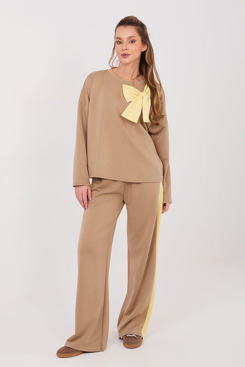 Woman wearing a beige outfit with a yellow bow and stripe on a white background