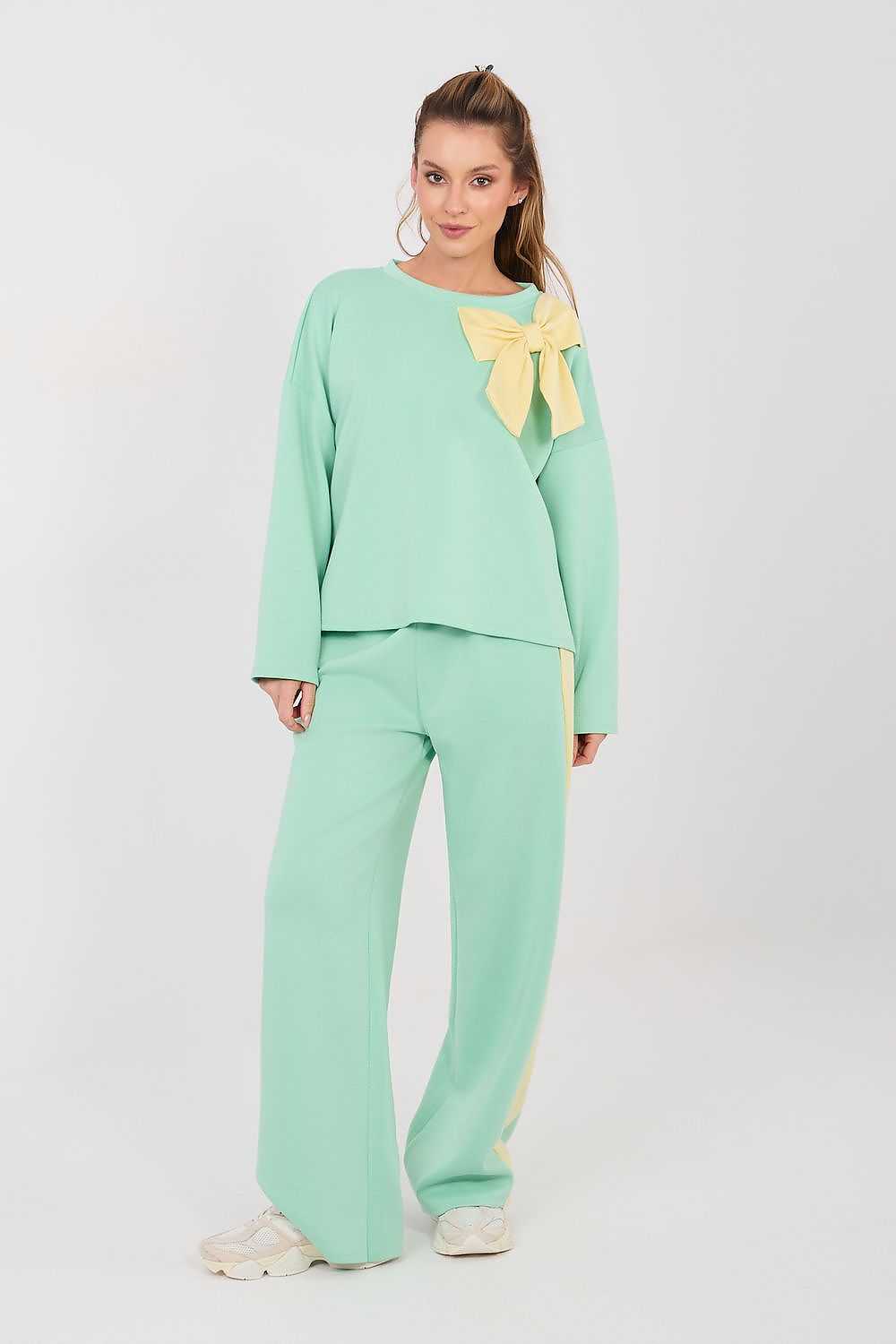 Woman wearing a mint green outfit with a yellow bow on a white background