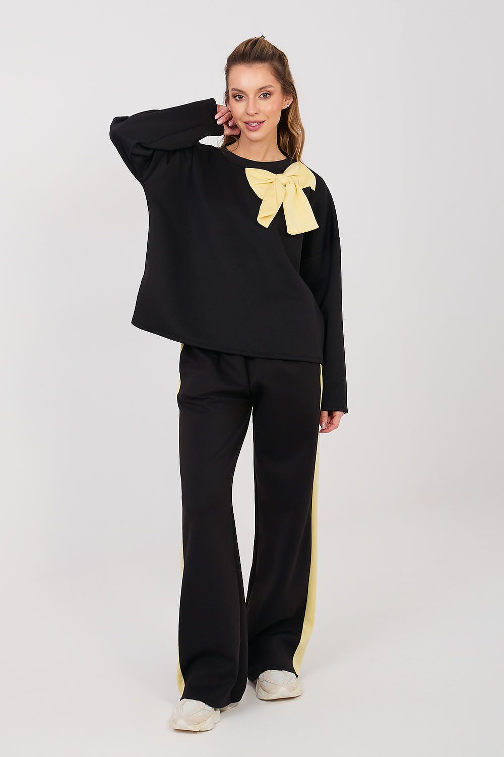 Woman wearing a black outfit with a yellow bow detail on a white background