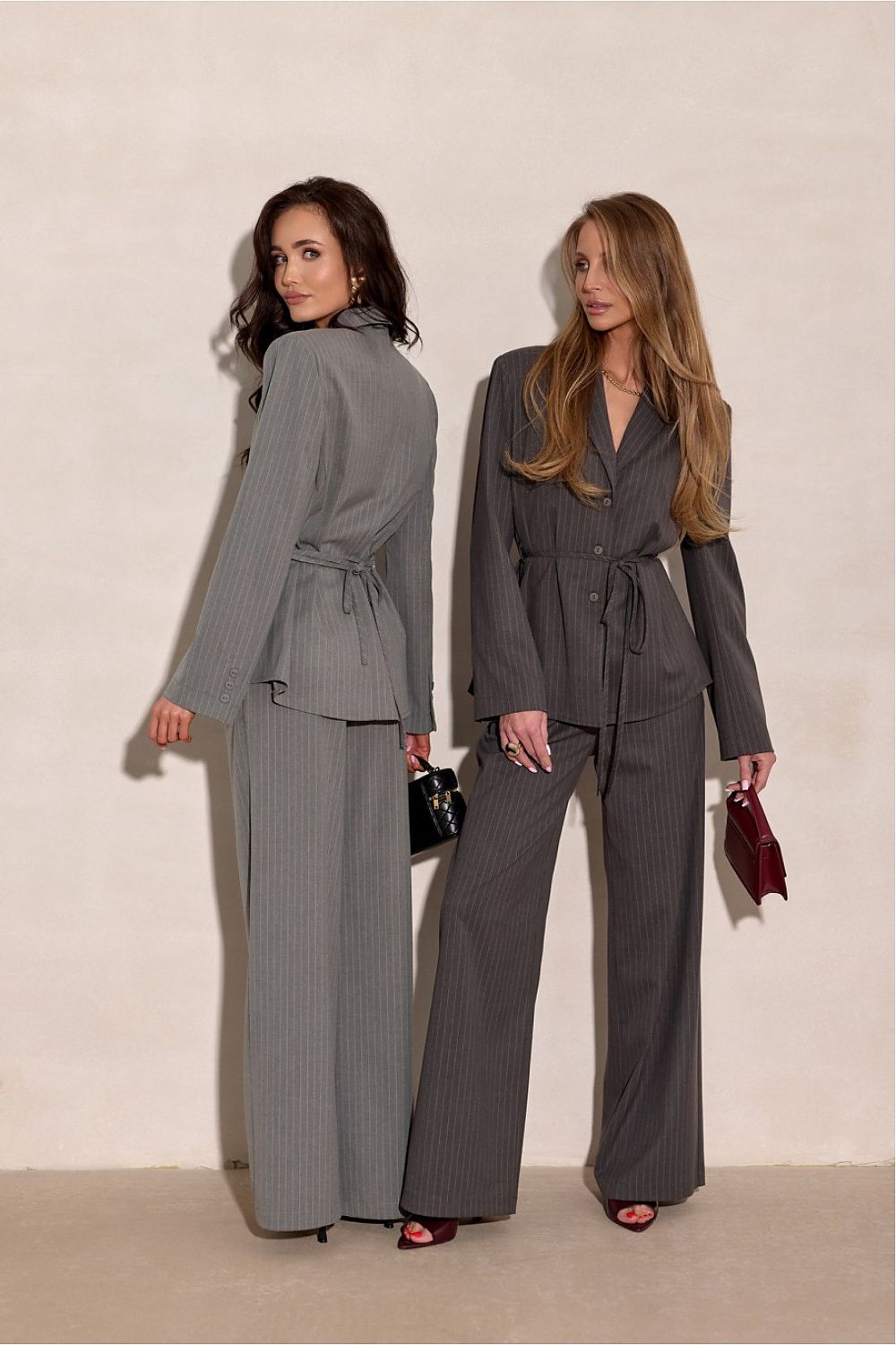 Two women wearing gray suits standing against a plain background
