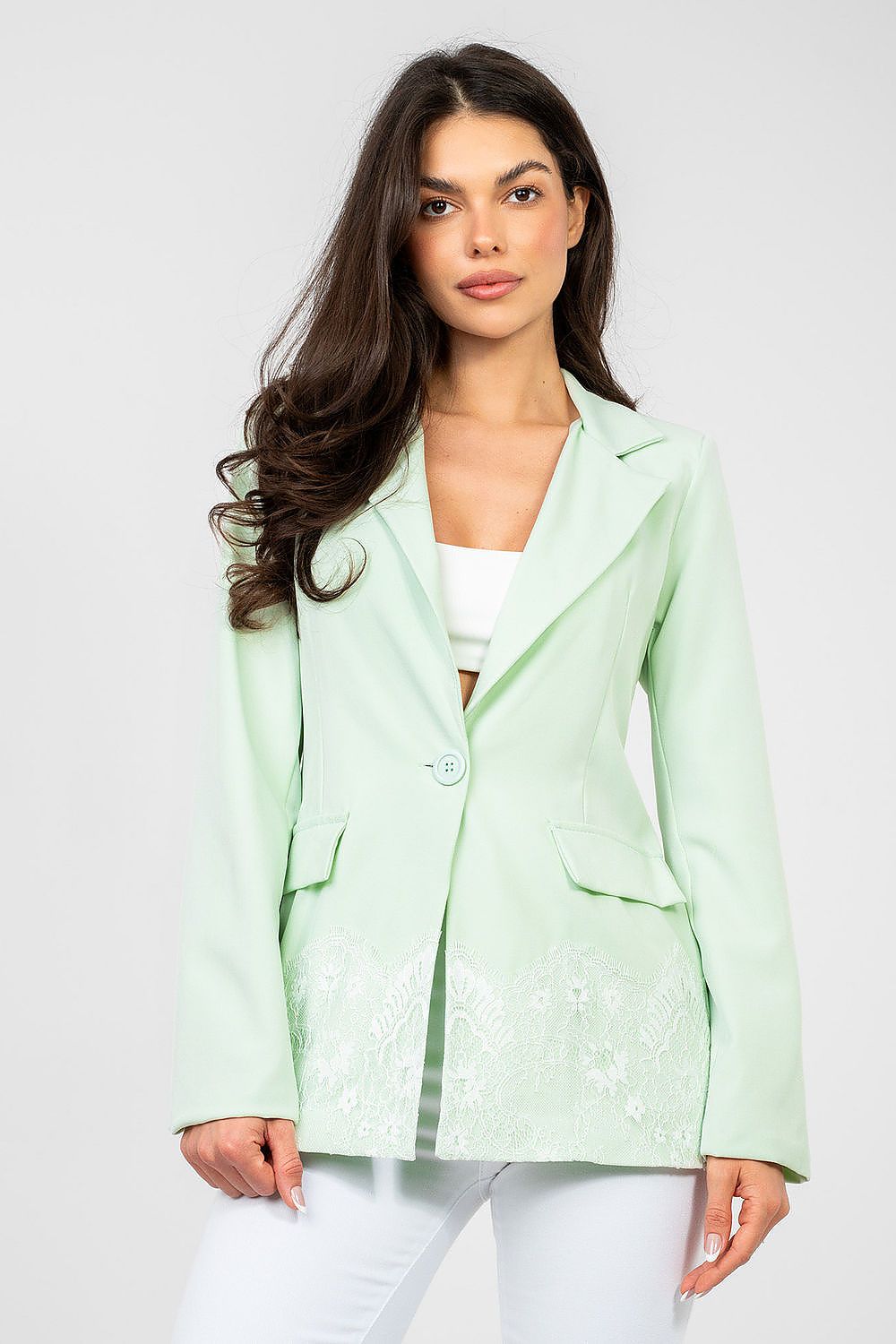 Woman wearing a light green blazer over a white top on a plain background