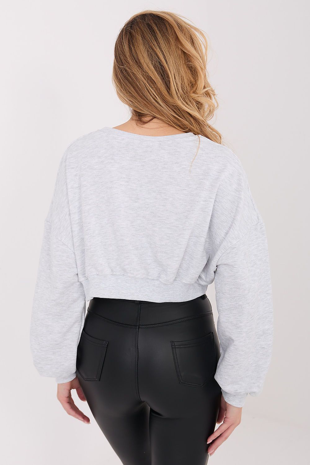 Person wearing a light gray sweater and black pants on a plain background