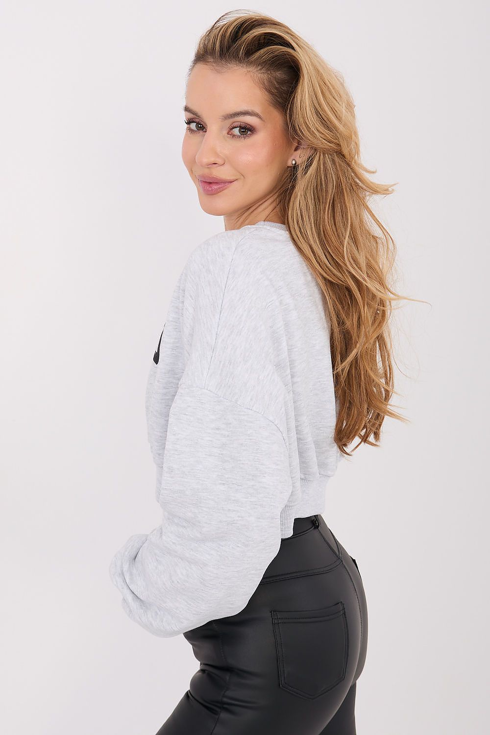 Woman wearing a light gray sweater and black pants on a white background