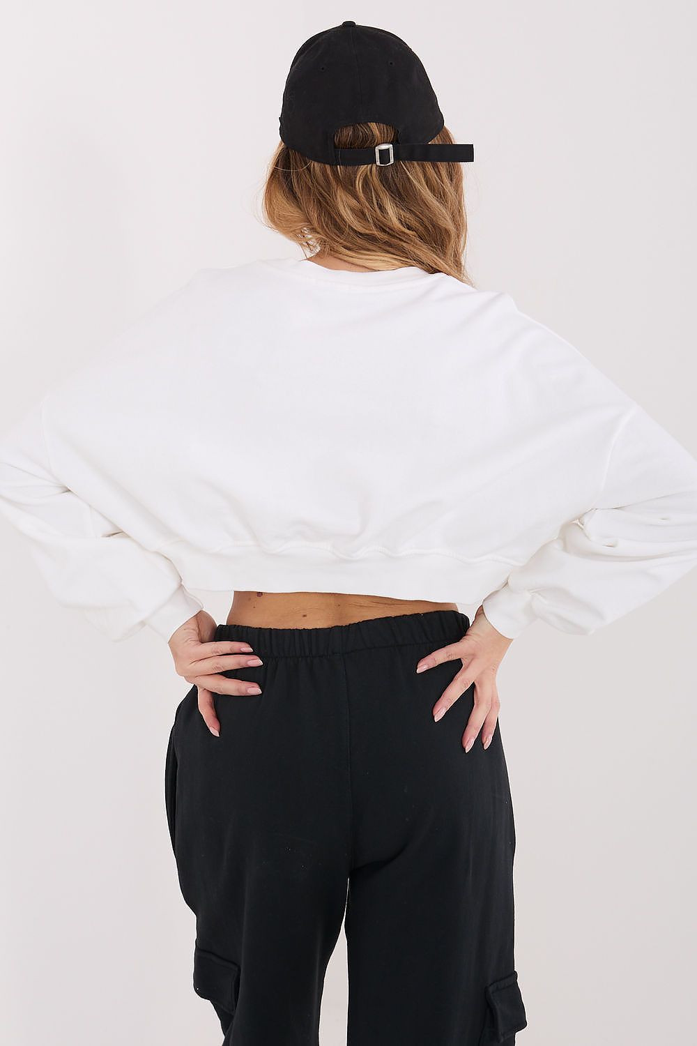Person wearing a white sweatshirt and black pants with a black cap on a white background