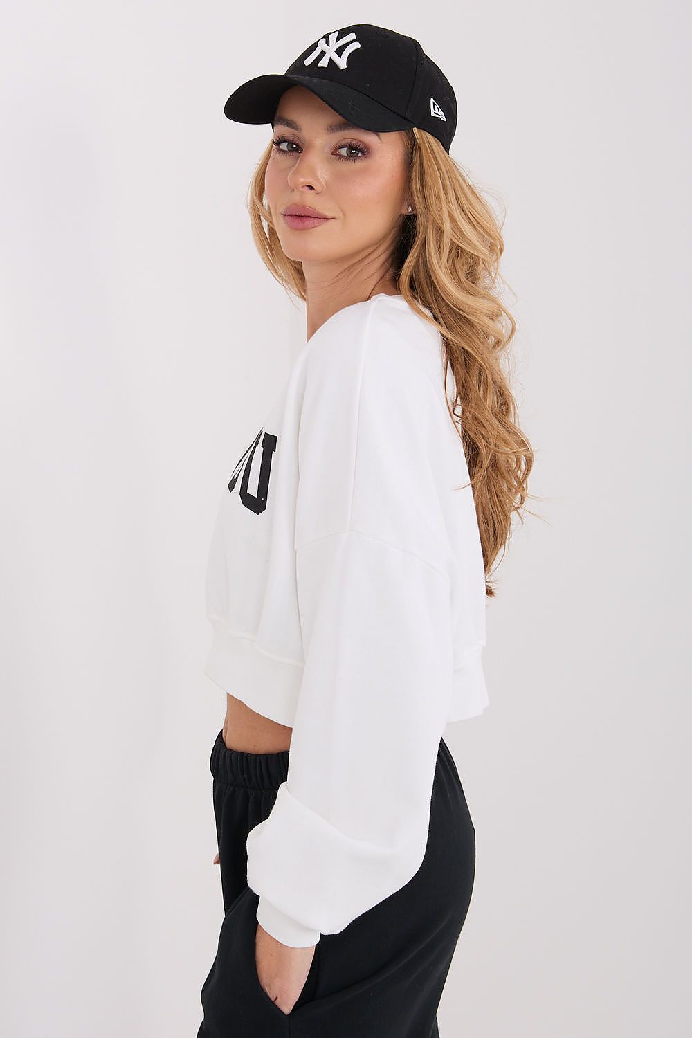 Woman wearing a white sweatshirt and black cap on a plain background