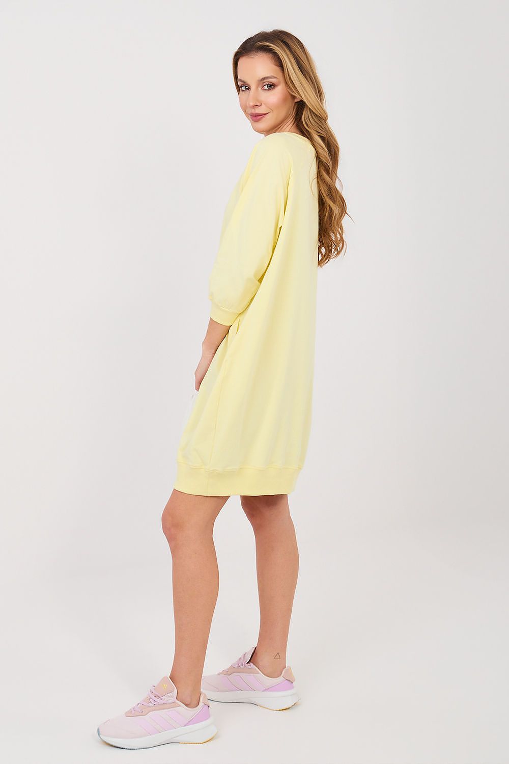 Woman wearing a yellow dress with pink sneakers on a white background
