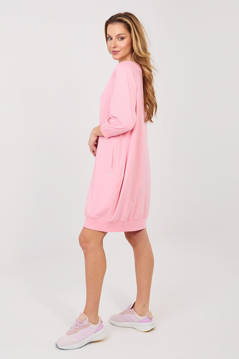 Woman wearing a pink dress with matching sneakers on a white background