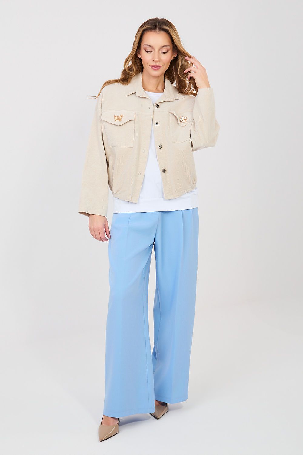 Woman wearing a beige jacket and light blue pants on a white background