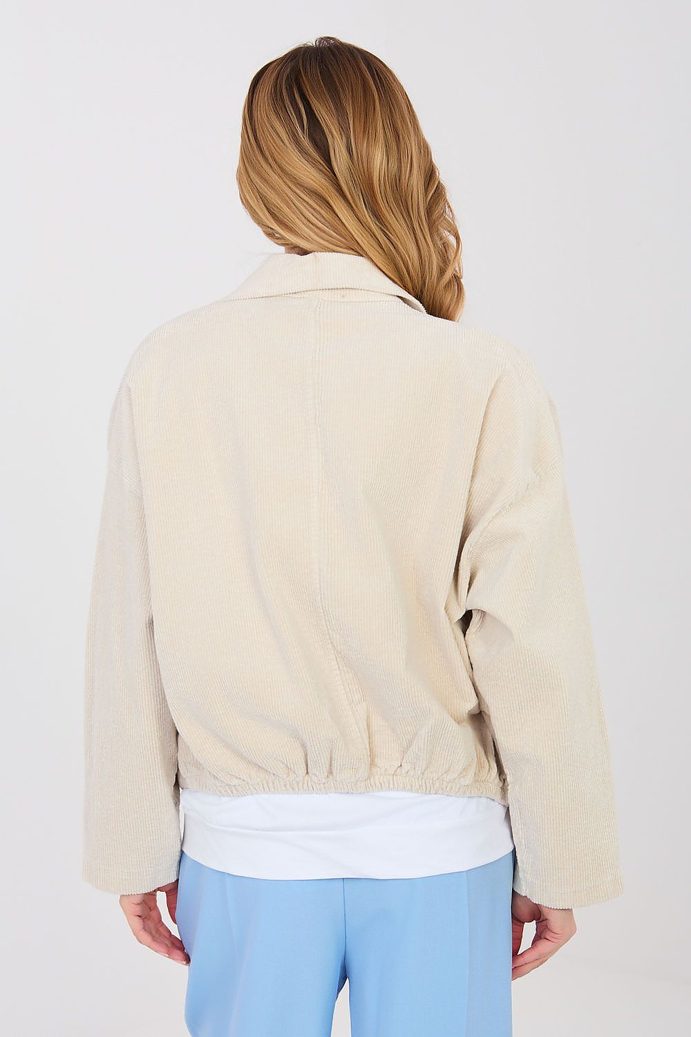 Person wearing a beige jacket, white shirt, and light blue pants on a plain background