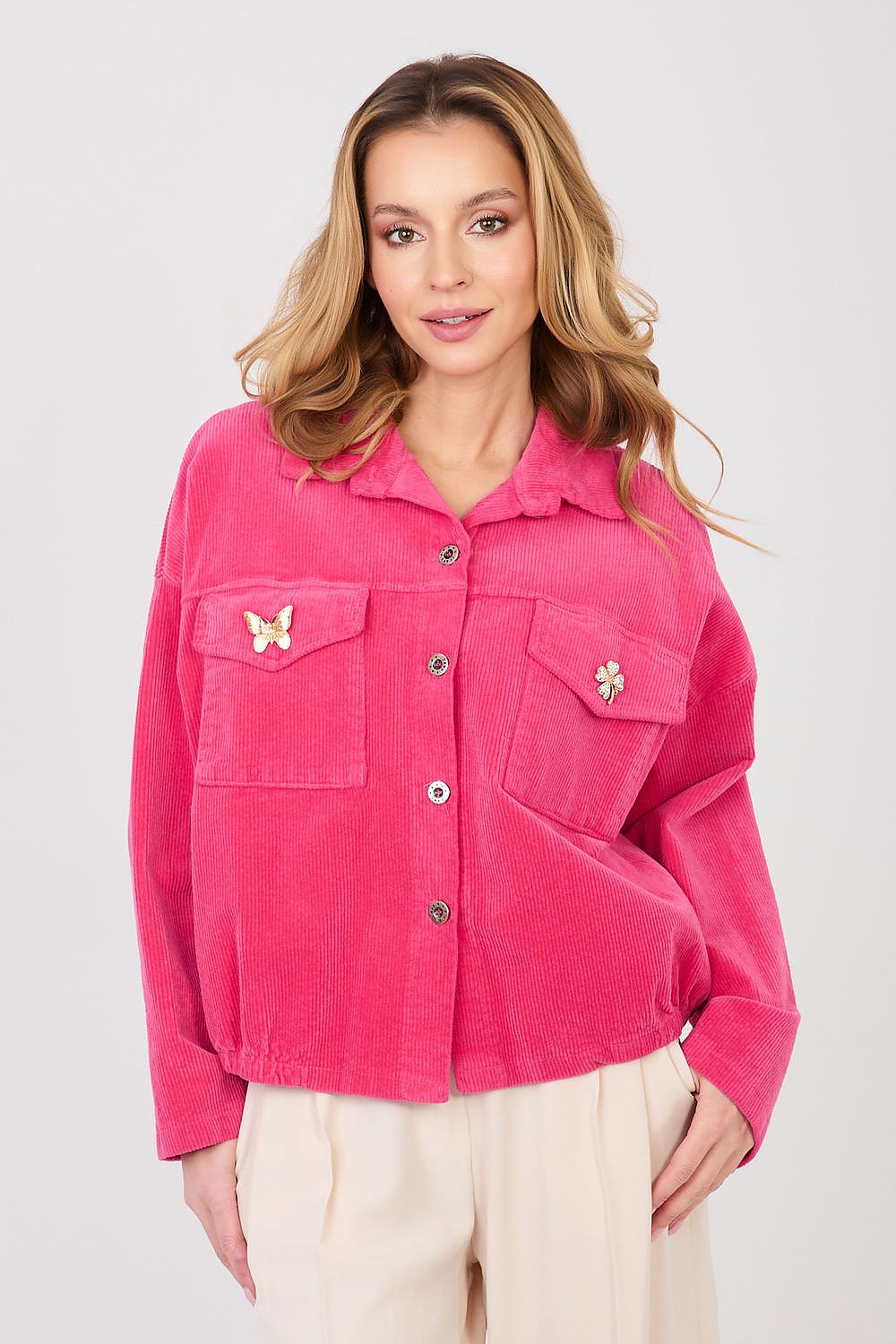 Woman wearing a bright pink jacket with butterfly patches on a plain background
