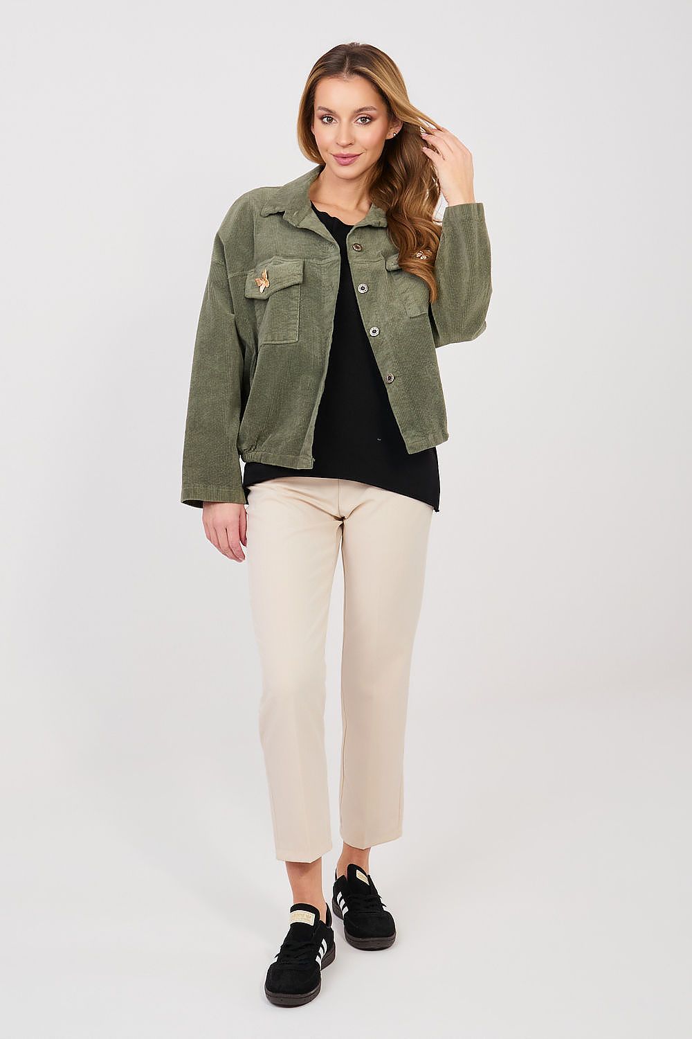 Woman wearing a green jacket, black shirt, beige pants, and black shoes on a white background