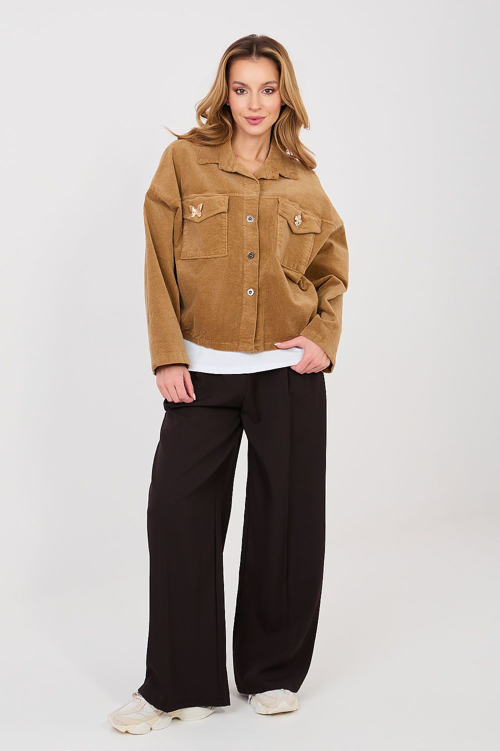 Woman wearing a tan jacket and black pants on a white background