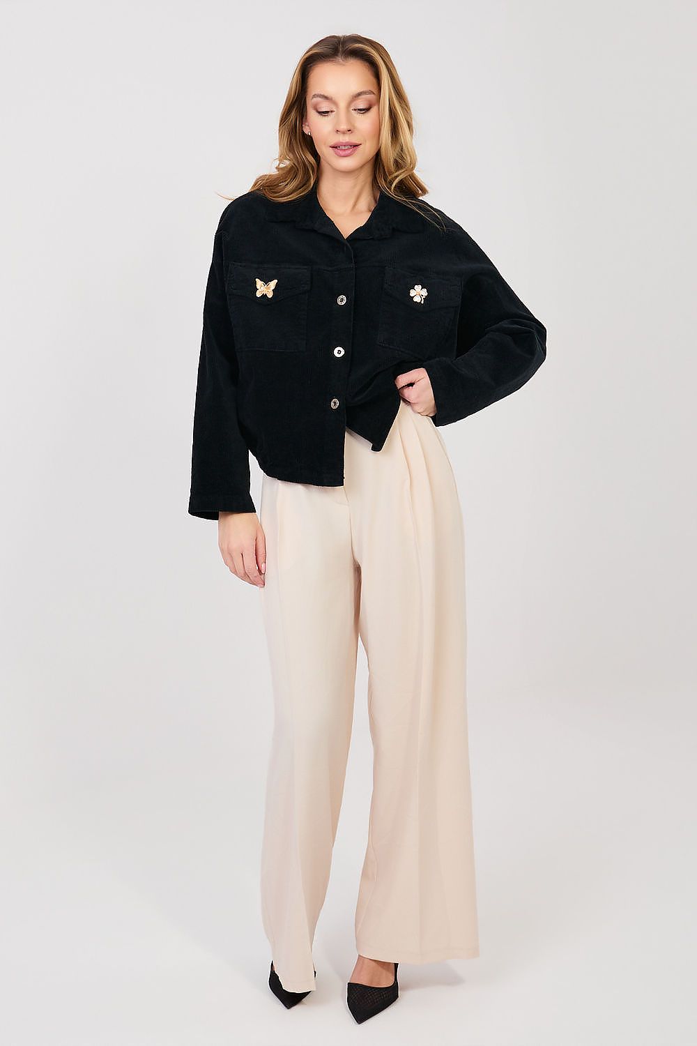 Woman wearing a black jacket with white buttons and beige pants on a white background