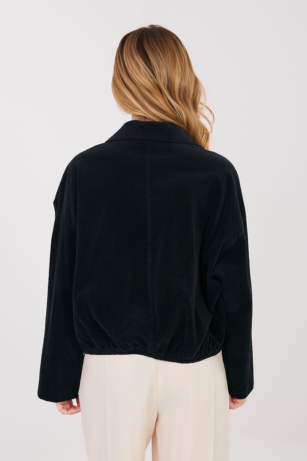 Person wearing a black jacket and white pants on a plain background