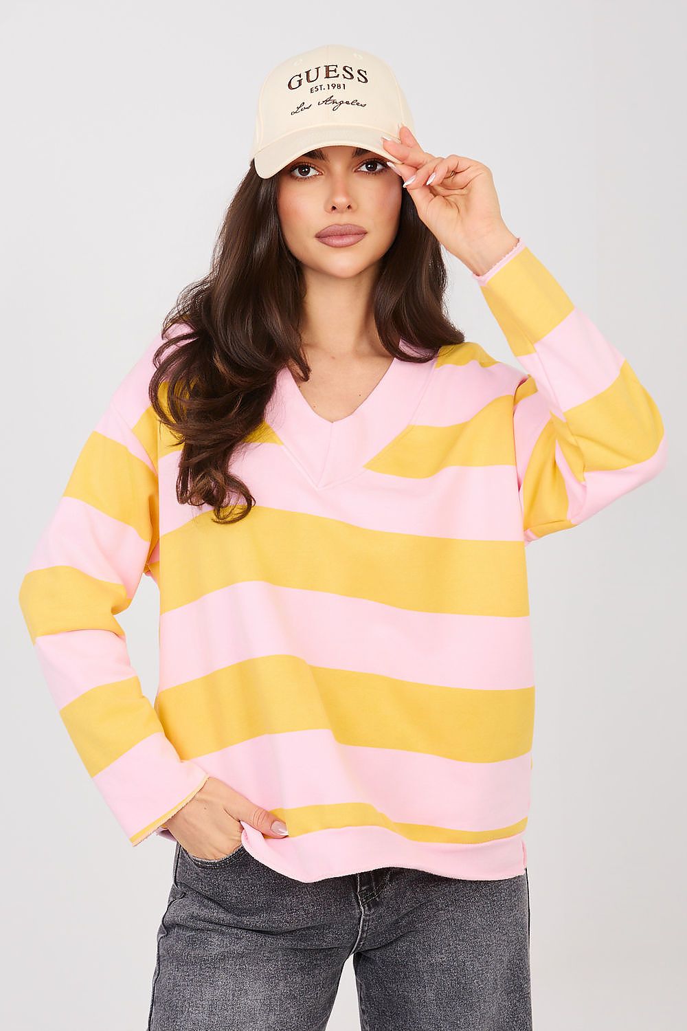 Woman wearing a yellow and pink striped sweater with a beige cap on a light gray background