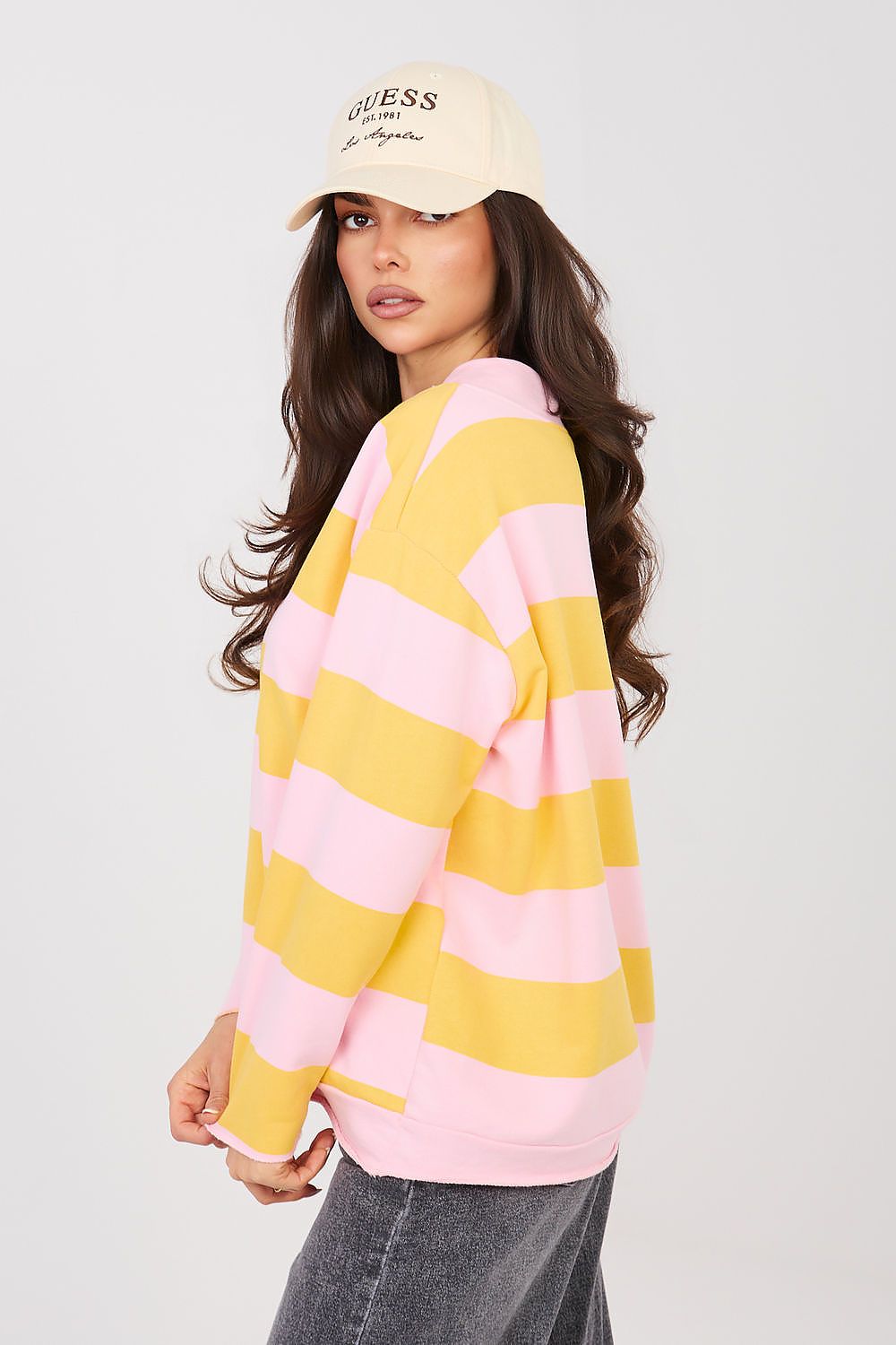 Woman wearing a yellow and pink striped sweater with a beige cap on a light gray background