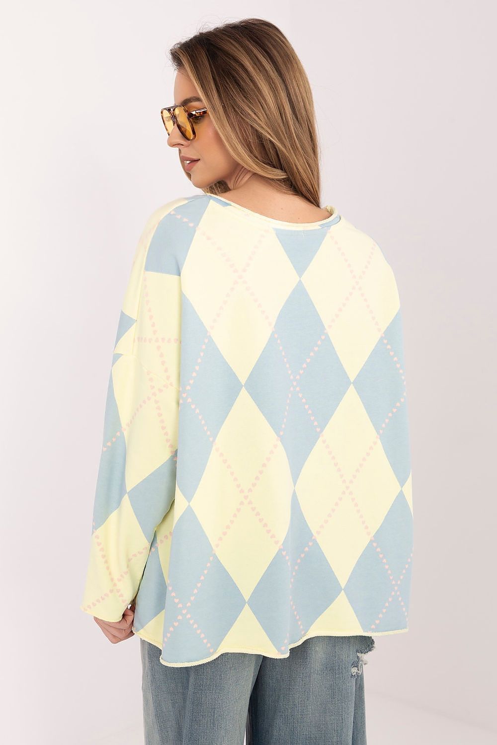 Woman wearing a pastel argyle sweater with blue and yellow diamond patterns on a white background.