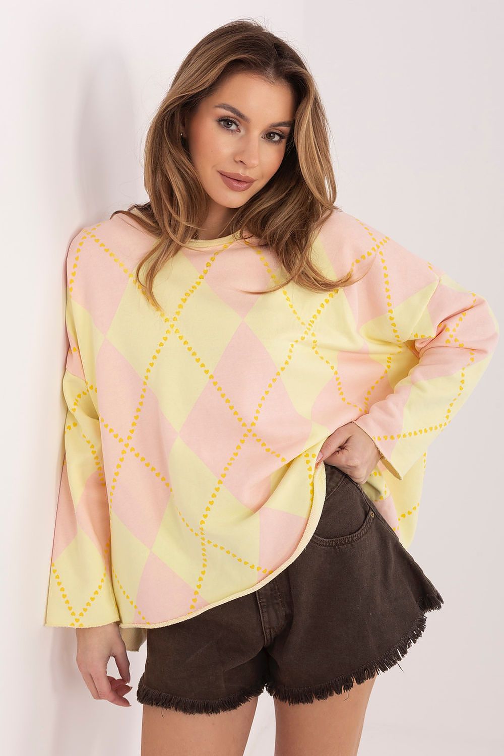 Woman wearing a pink and yellow patterned top with brown shorts on a white background