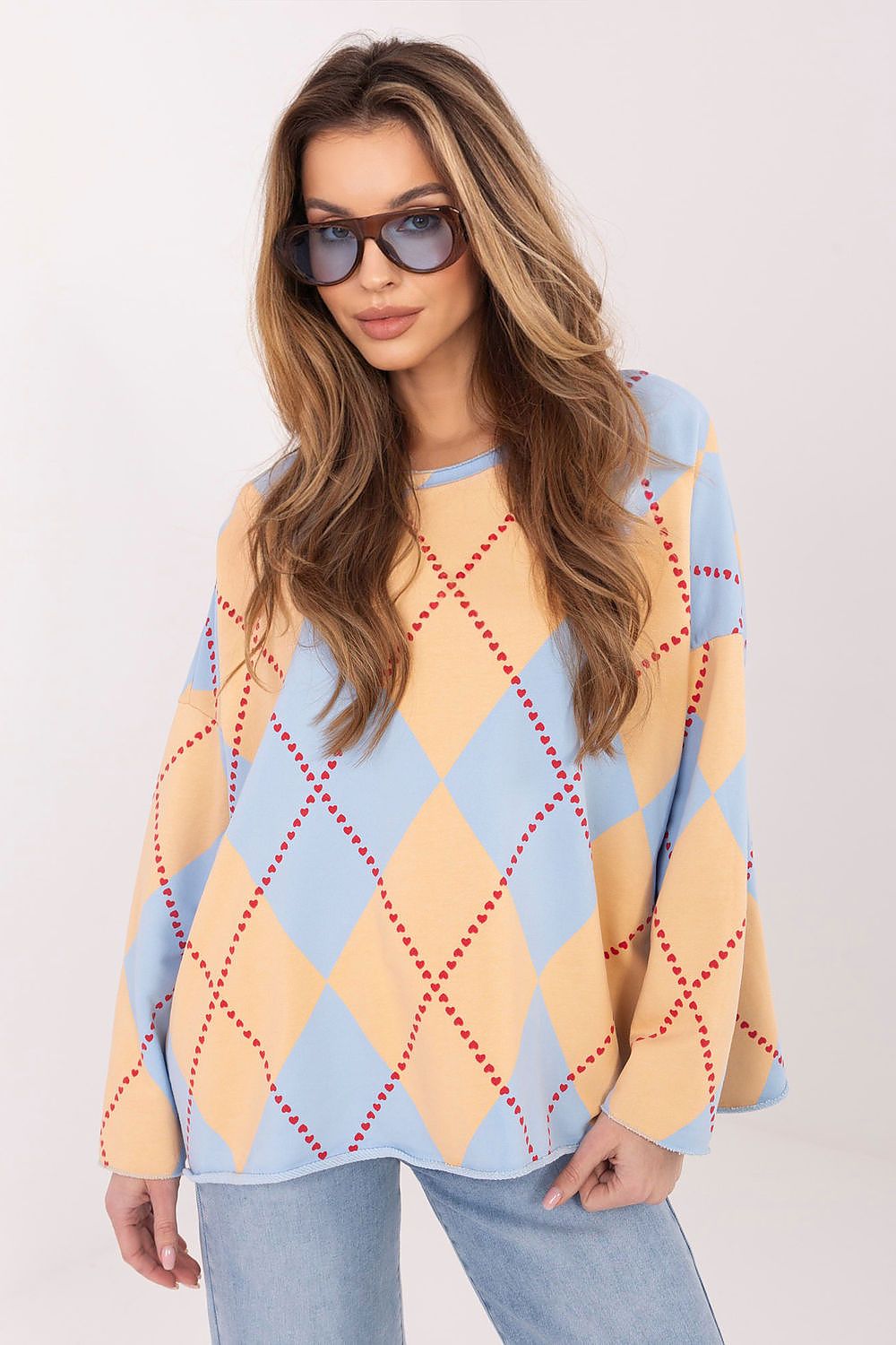 Woman wearing a yellow and blue argyle sweater with sunglasses on a white background
