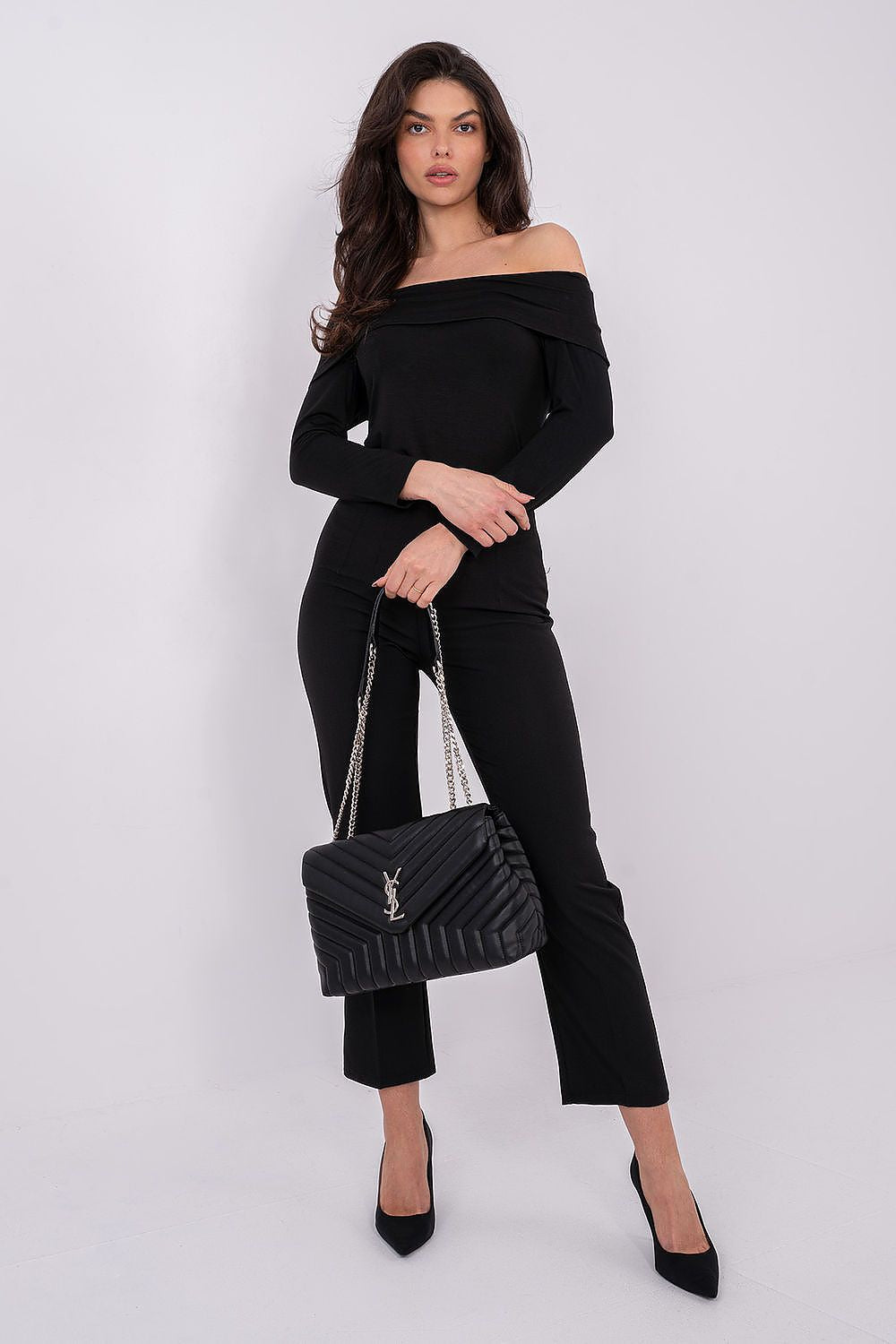 Woman in black outfit holding a black handbag against a white background