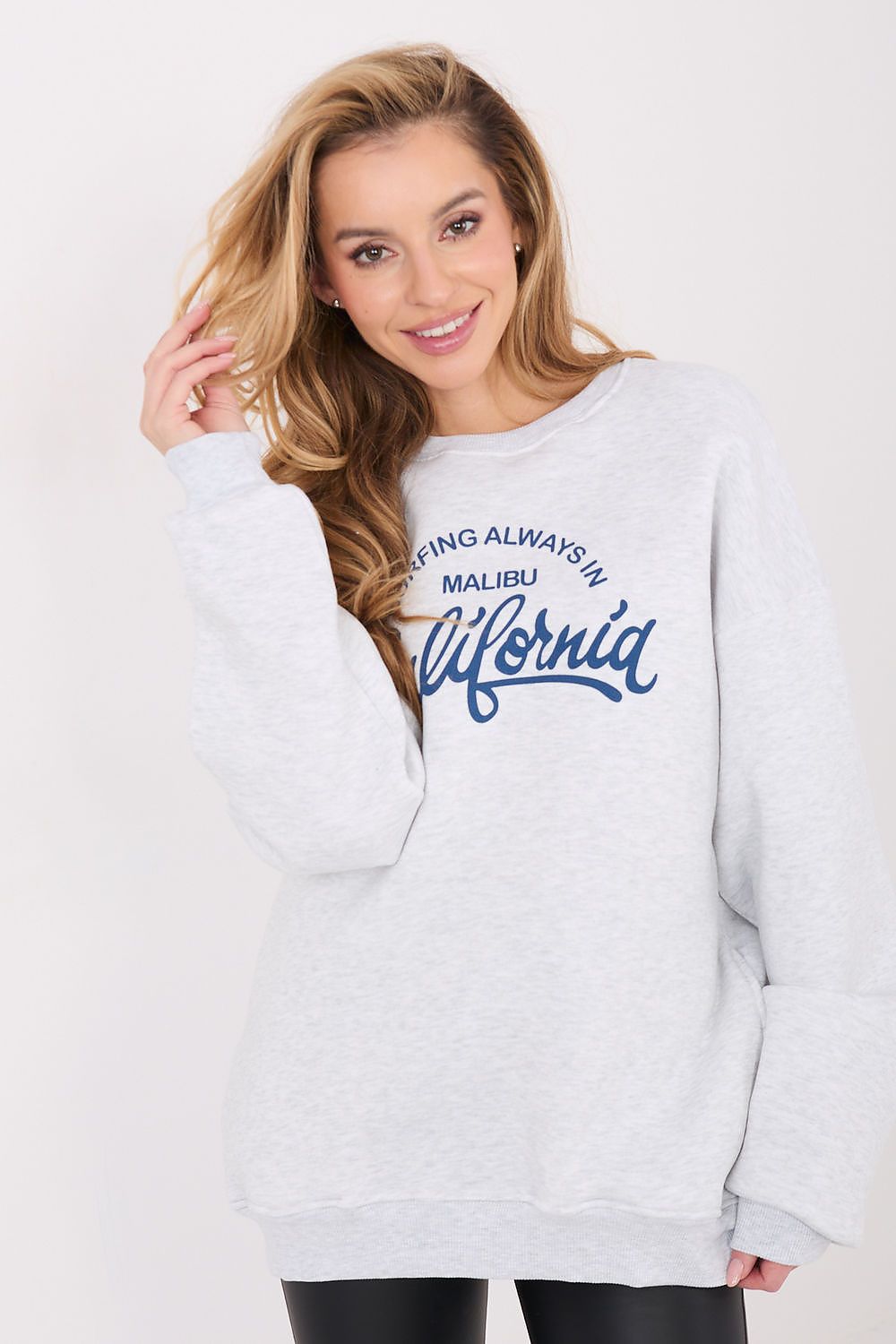 Woman wearing a gray sweatshirt with text, standing against a white background