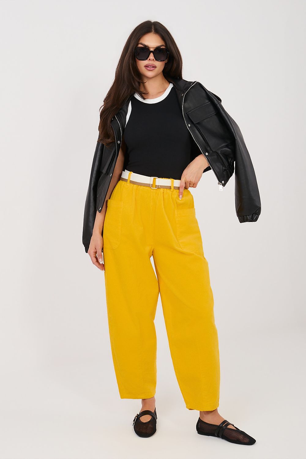 Woman wearing a black leather jacket, black top, and yellow pants on a white background
