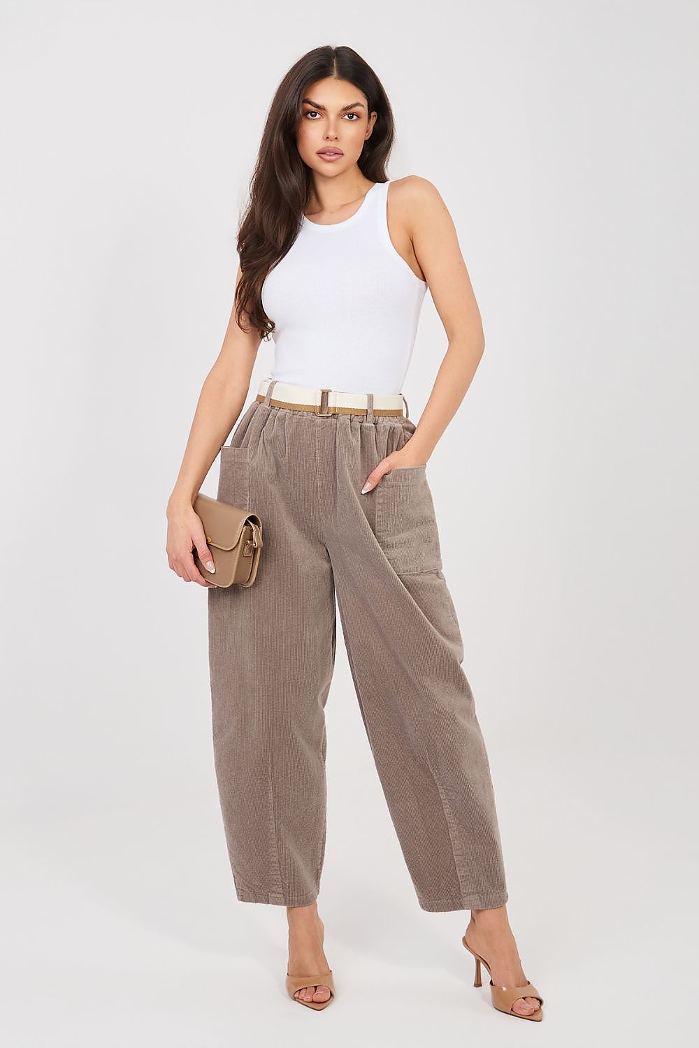 Woman wearing a white sleeveless top and brown high-waisted pants on a white background