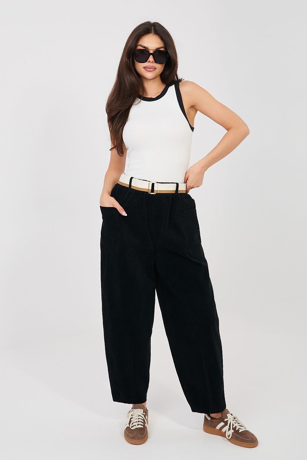 Woman wearing a white sleeveless top and black high-waisted pants on a white background