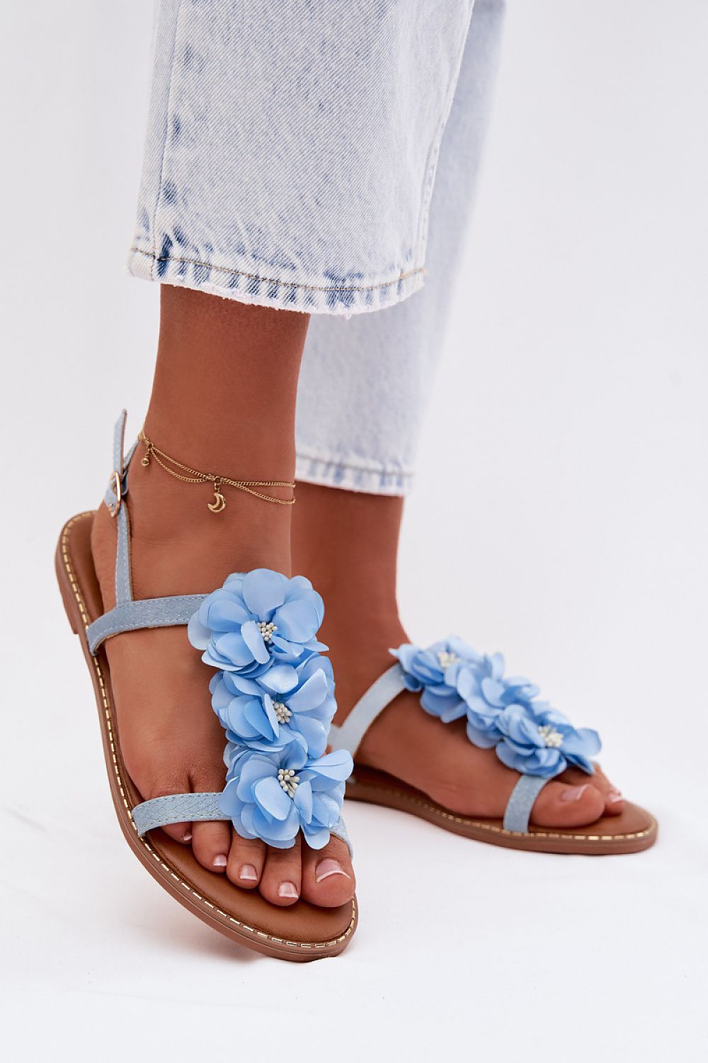 Blue floral sandals worn with light blue jeans on a white background