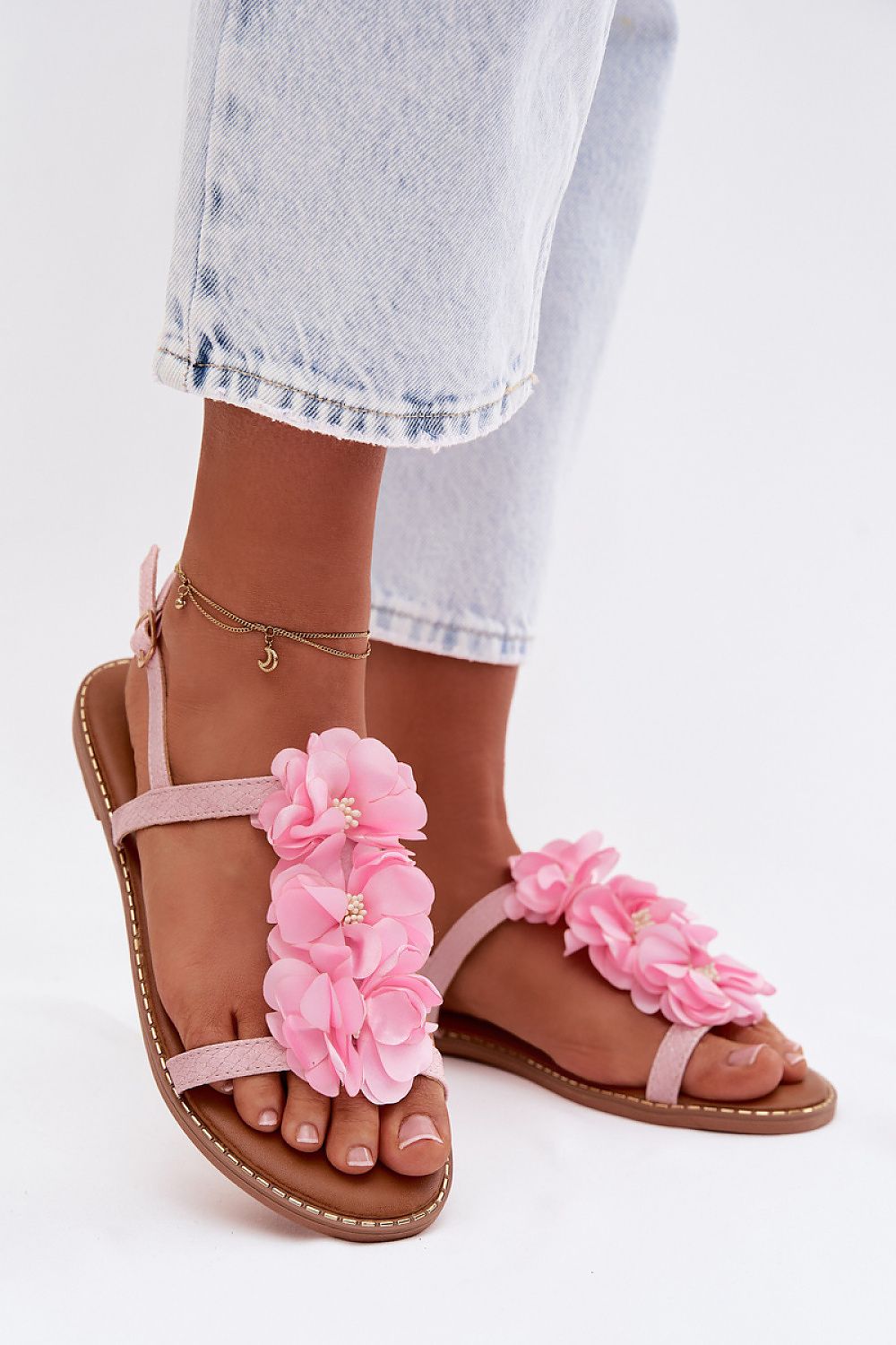 Pink floral sandals worn with light blue jeans on a white background