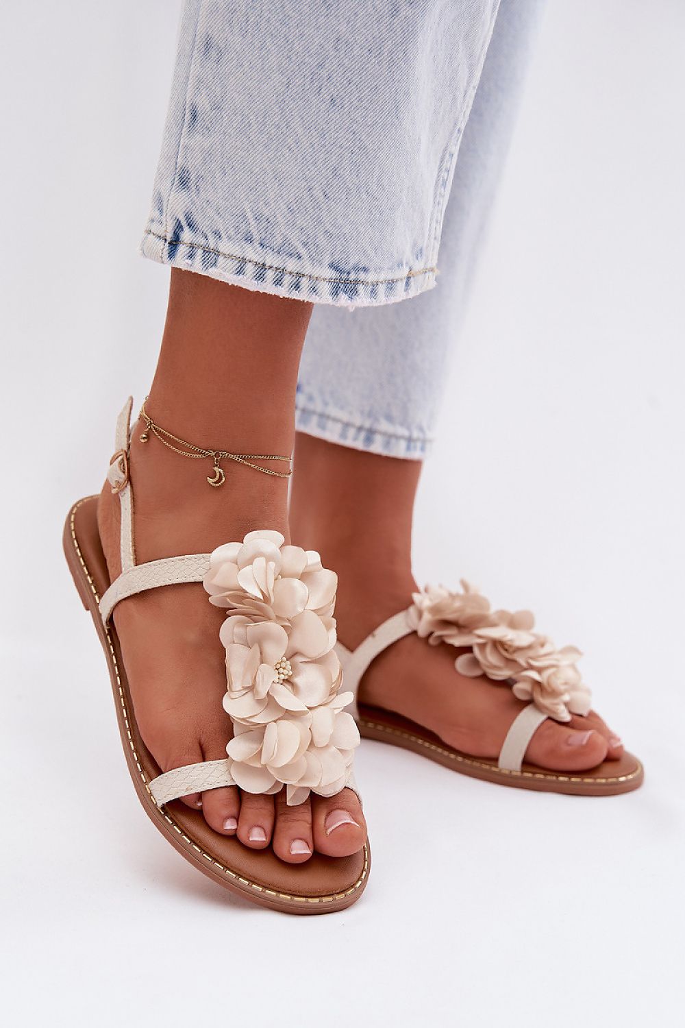 Beige sandals with floral decorations worn by a person on a white background