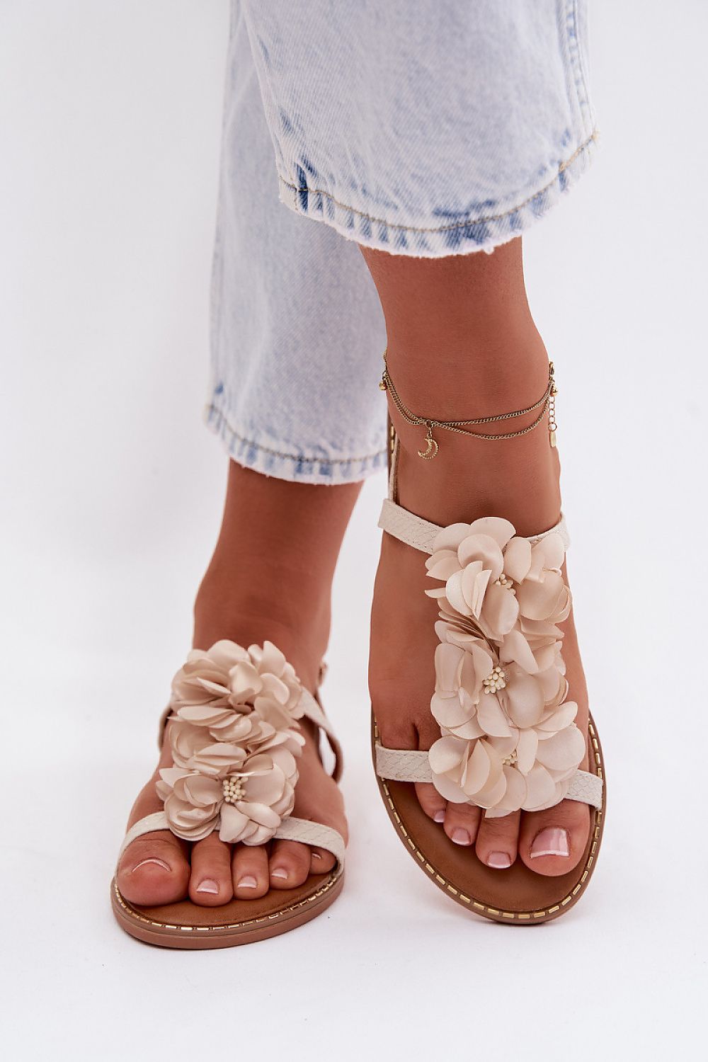 Beige floral sandals worn with light blue denim shorts on a white background