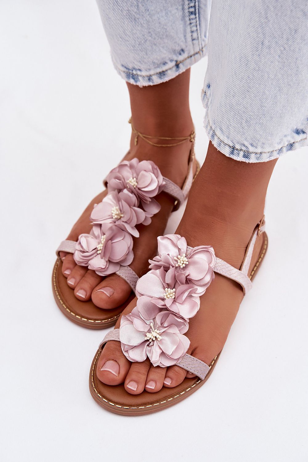 Pink floral sandals worn with light blue jeans on a white background