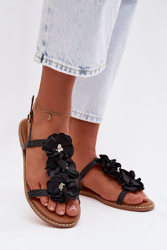 Black floral sandals worn with light blue jeans on a white background