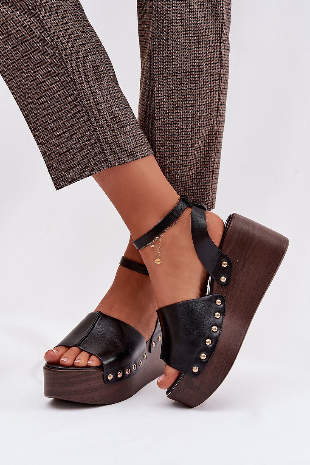 Black platform sandals with wooden soles worn with plaid pants on a white background